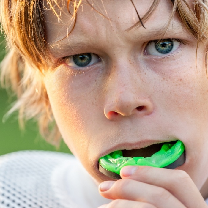 Boy putting green athletic mouthguard in his mouth