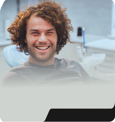 Young man with curly brown hair smiling in dental chair