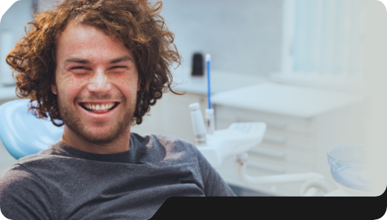 Young man with curly brown hair smiling in dental chair