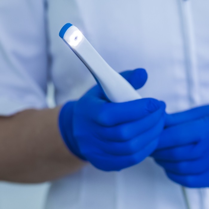 Gloved hands holding a thin white intraoral camera