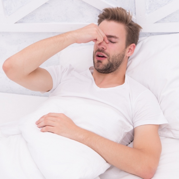 Yawning man laying in bed pinching bridge of nose