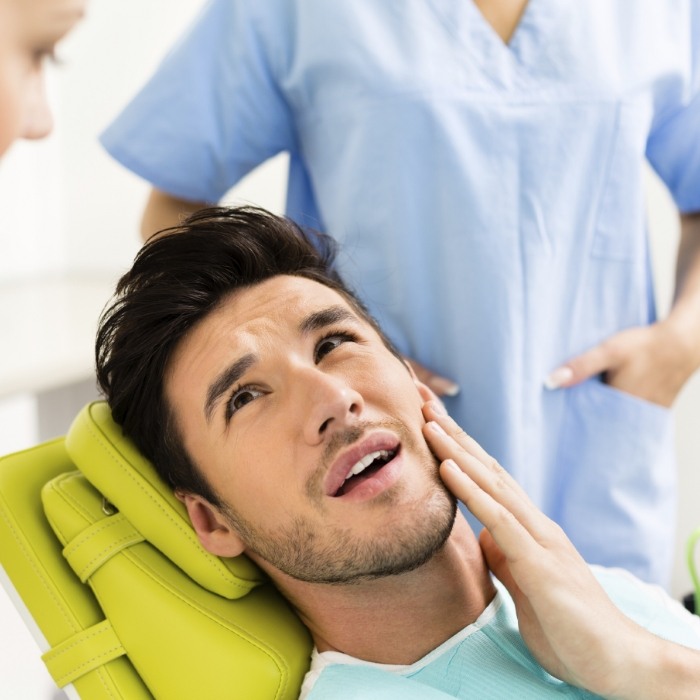 Man in dental chair holding his jaw in pain