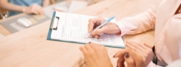 Dental patient signing dental insurance form on clipboard