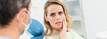 Woman in dental chair holding her cheek in pain