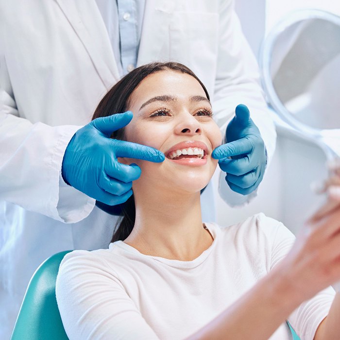 Dentist showing patient their smile in reflection of handheld mirror