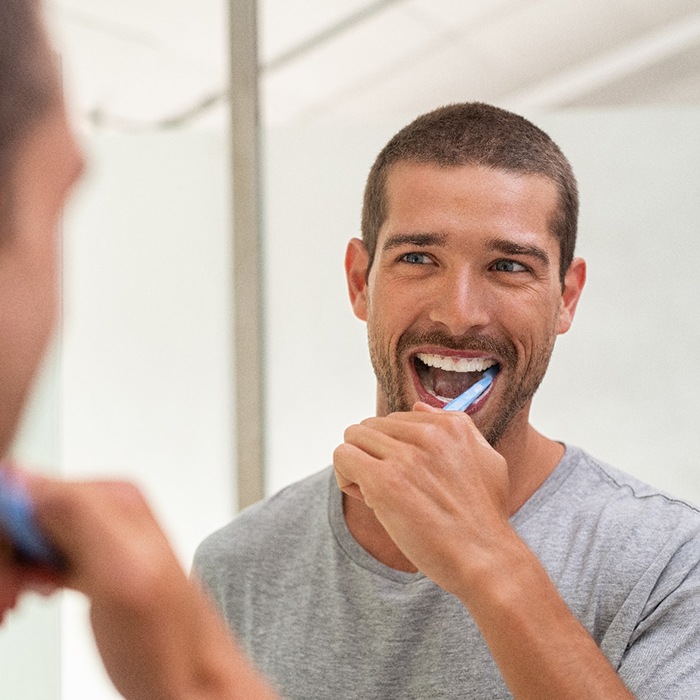 Man smiling while brushing his teeth in bathroom