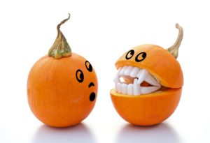Two pumpkins with faces drawn on them and one of them wearing fake vampire teeth